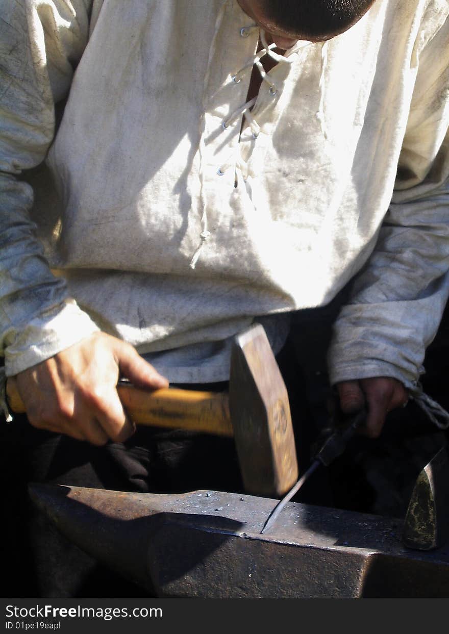 A young blacksmith in white shirt forging a nail. A young blacksmith in white shirt forging a nail