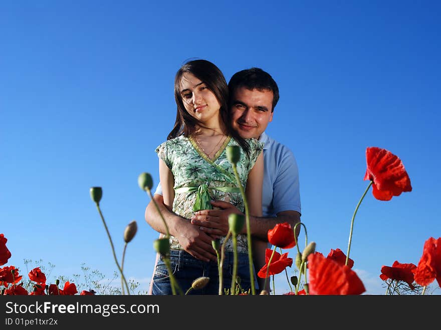 A beautiful young couple standing on a field filled with red poppies. A beautiful young couple standing on a field filled with red poppies