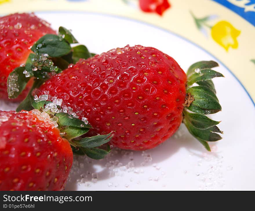 Three fresh ripe strawberries sprinkled with course white sugar on colorful flower pattern decorated dish. Three fresh ripe strawberries sprinkled with course white sugar on colorful flower pattern decorated dish.