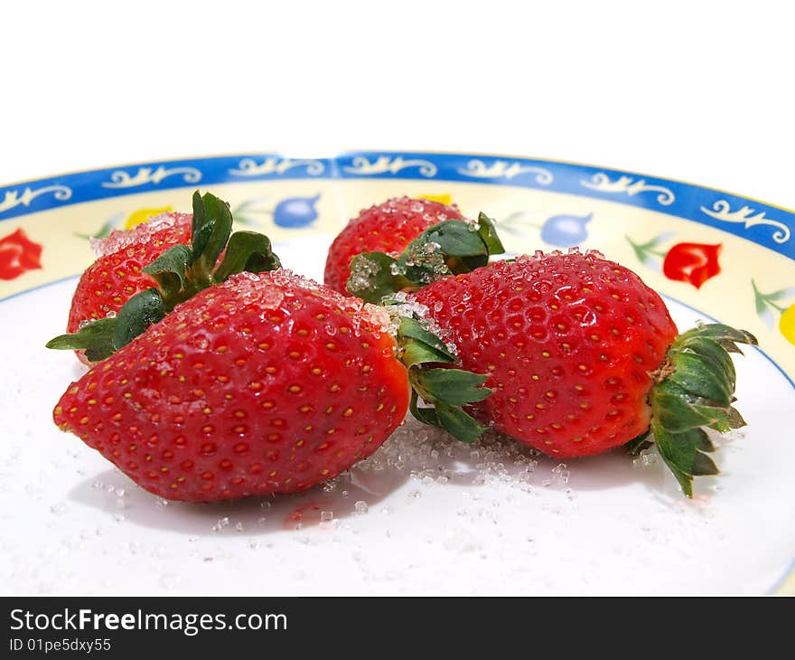 Front view of four fresh ripe strawberries sprinkled with course white sugar on colorful flower pattern decorated dish. Front view of four fresh ripe strawberries sprinkled with course white sugar on colorful flower pattern decorated dish.