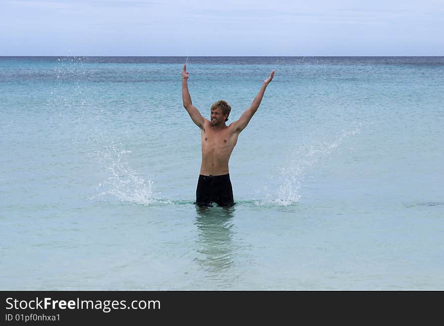 A man standing in the ocean sends sprays of water into the air. A man standing in the ocean sends sprays of water into the air.