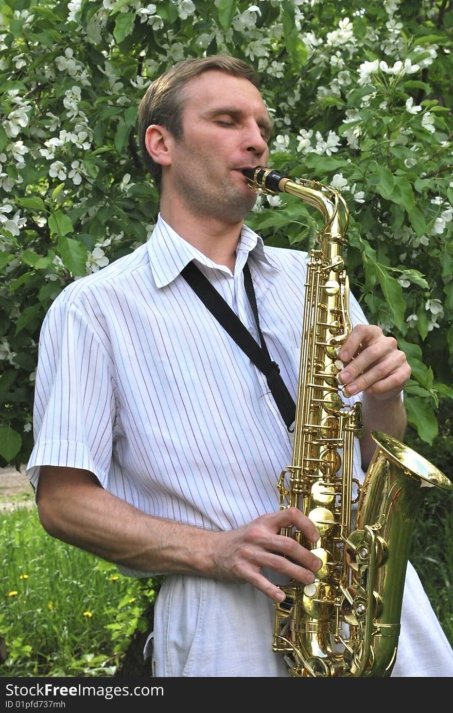 The man with saxophone on the background of the flowering tree