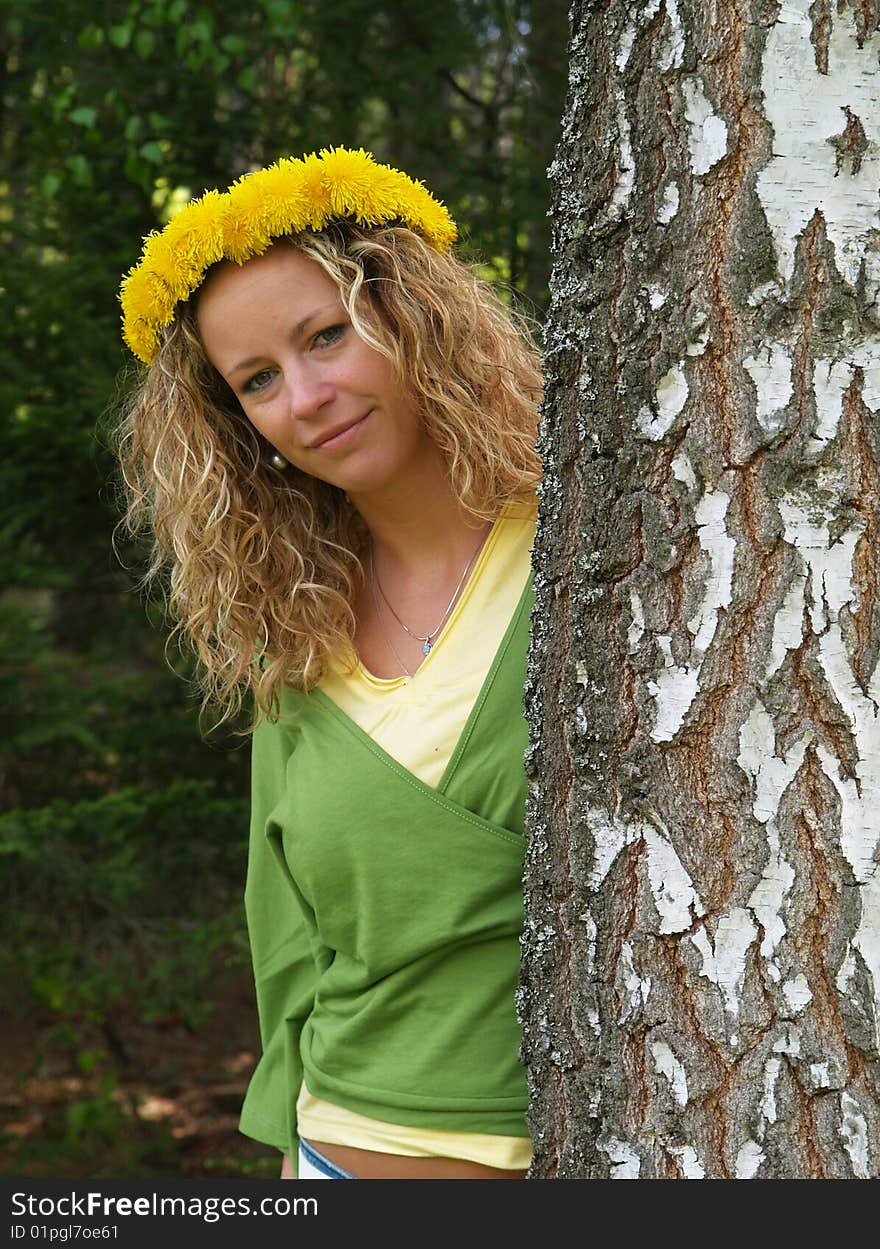 Curly girl with dandelion chain on head standing by birch tree