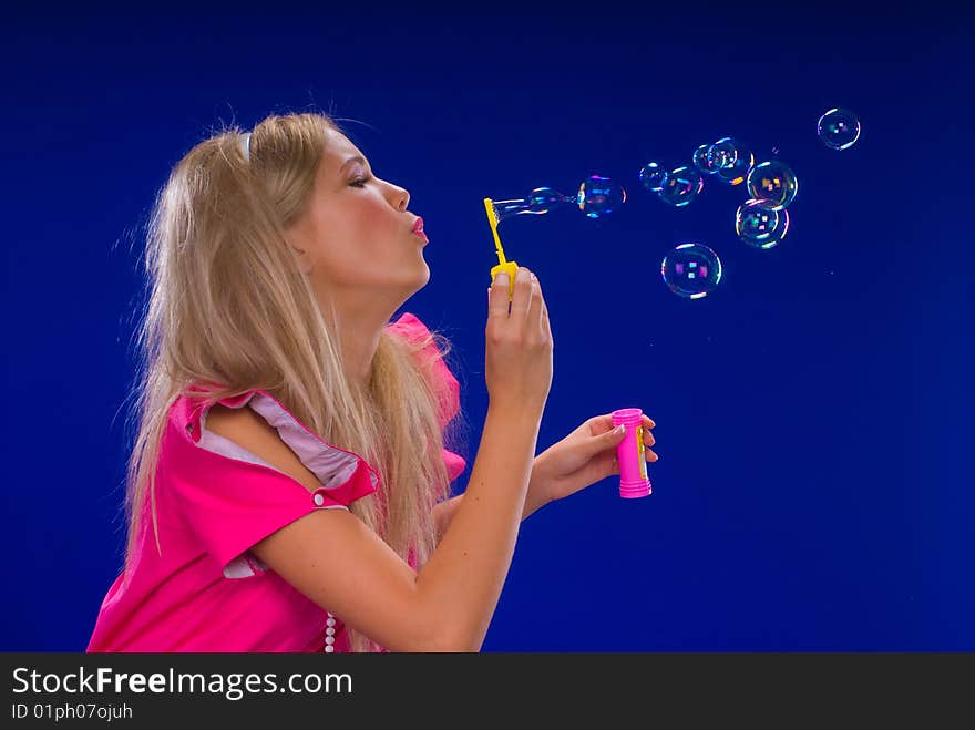 Young beautiful blond inflate soap bubbles on a blue background