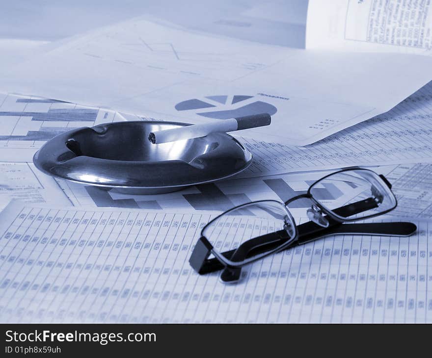 Ashtray, cigarette and glasses on financial documents. Toned blue. Shallow DOF.