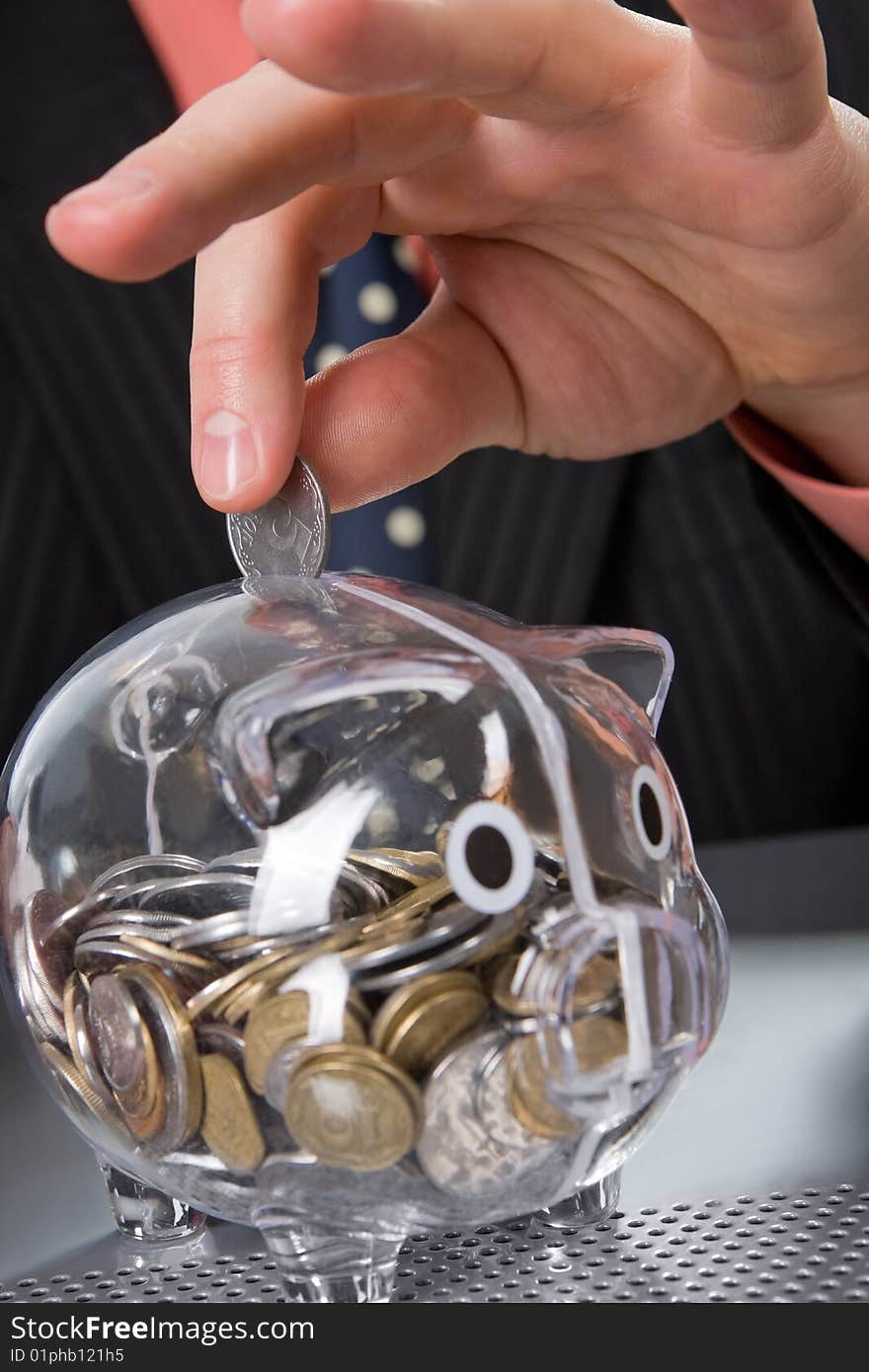 Businessman's hand inserting coin into transparent piggy bank