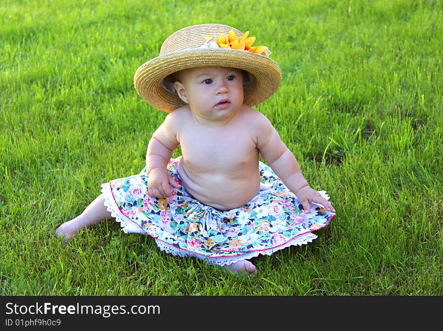 Baby girl wearing big hat sits on green grass