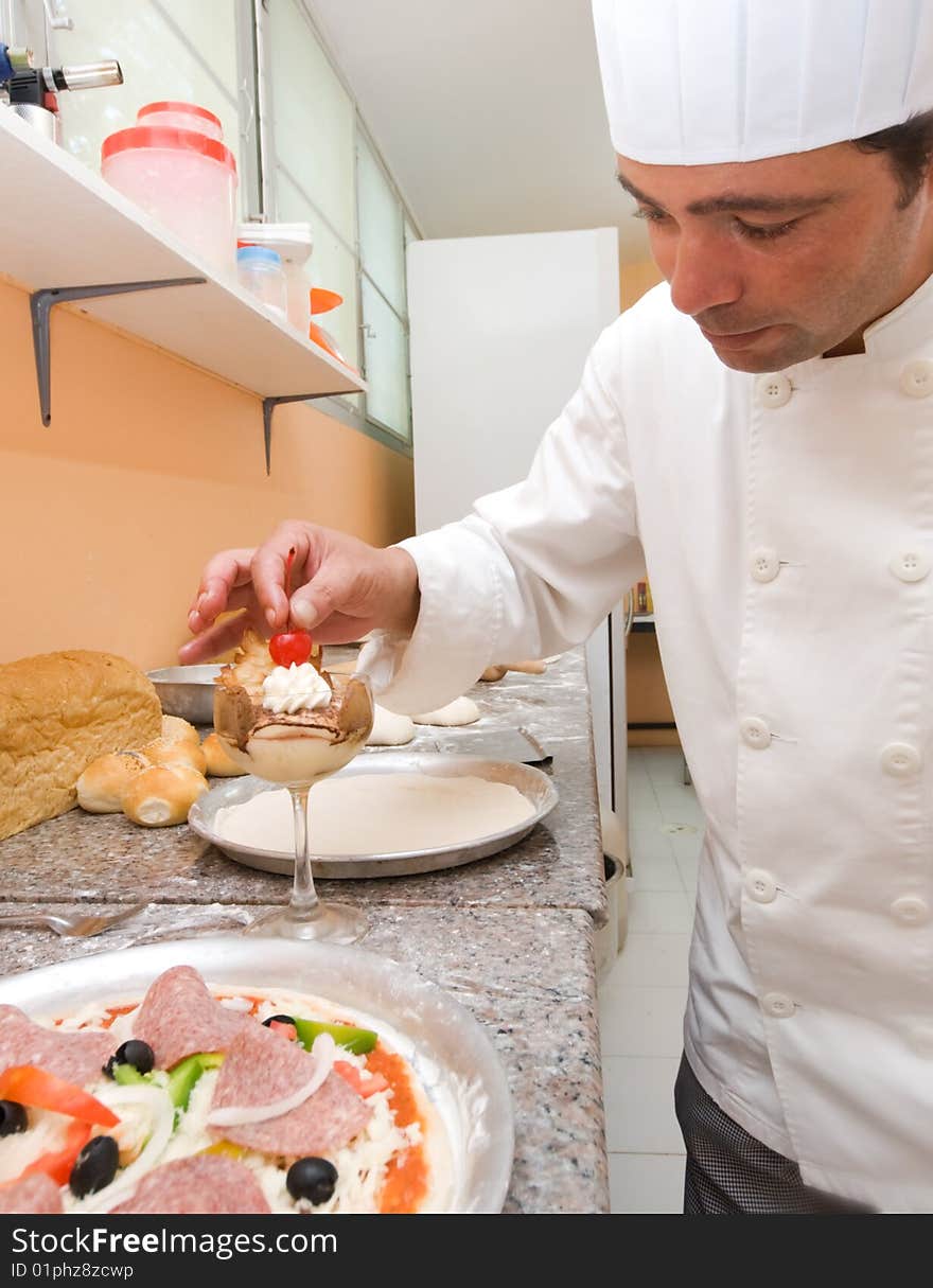 A pastry chef putting a cherry on top of a dessert in a restaurant kitchen. A pastry chef putting a cherry on top of a dessert in a restaurant kitchen