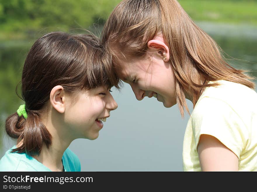 Close-up of two young smiling girls standing face-to-face with closed eyes on nature background. Close-up of two young smiling girls standing face-to-face with closed eyes on nature background