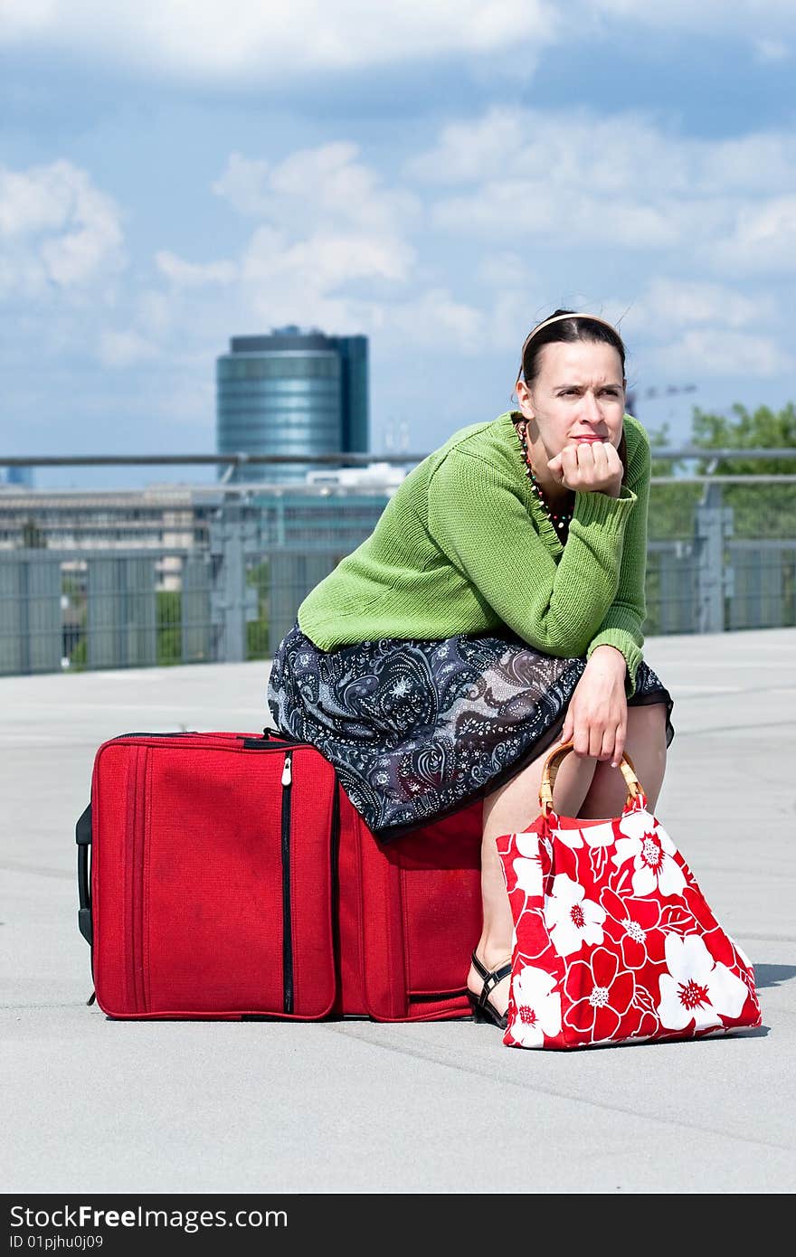 A woman sitting on a suitcase in an urban setting. A woman sitting on a suitcase in an urban setting.