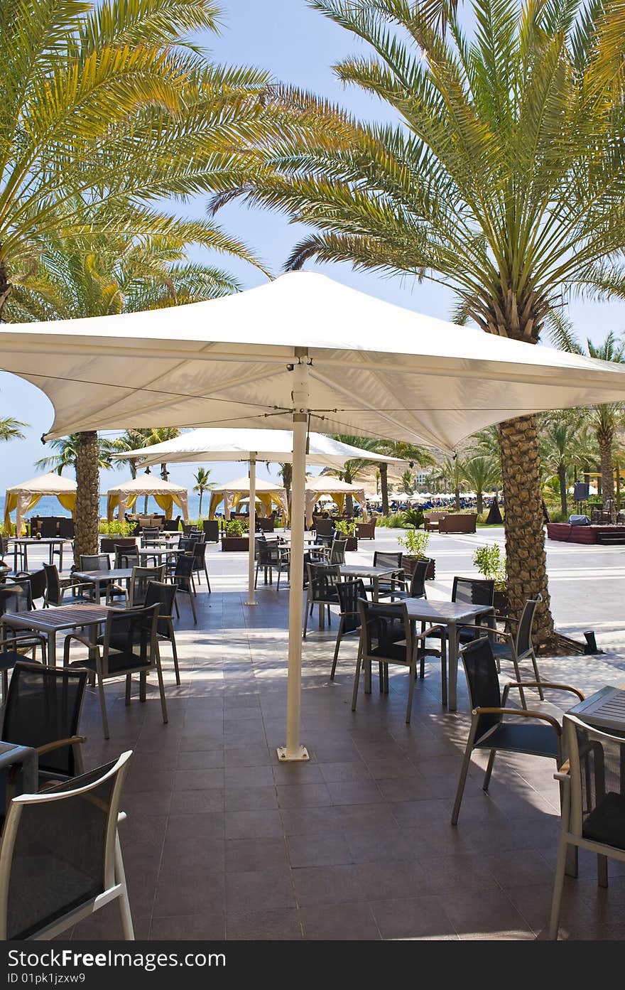 An outside restaurant at a hotel with nice place settings, surrounded by palm trees.