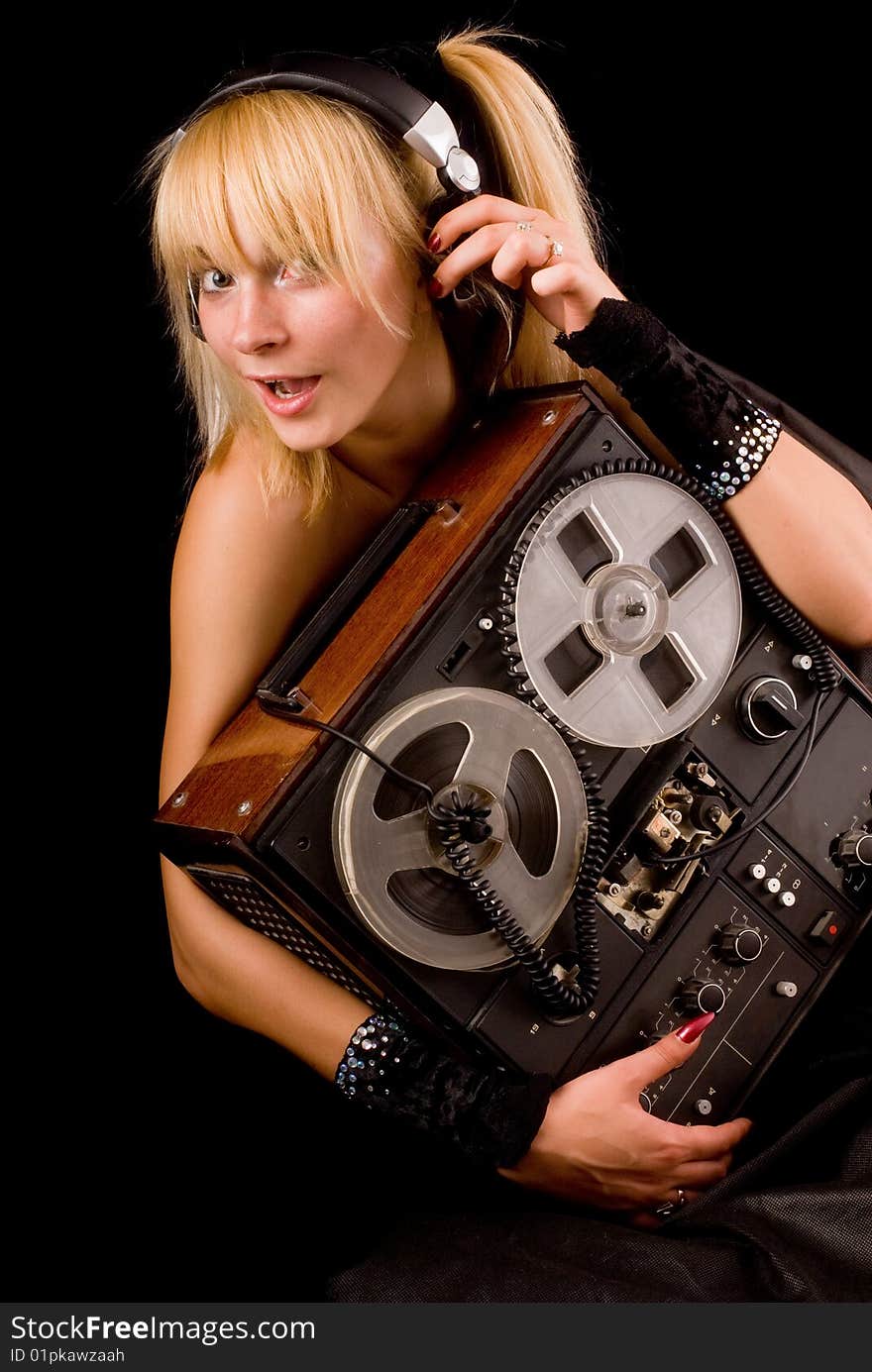 A young beautiful blonde with an old tape in the hands and the headphones on a black background. A young beautiful blonde with an old tape in the hands and the headphones on a black background