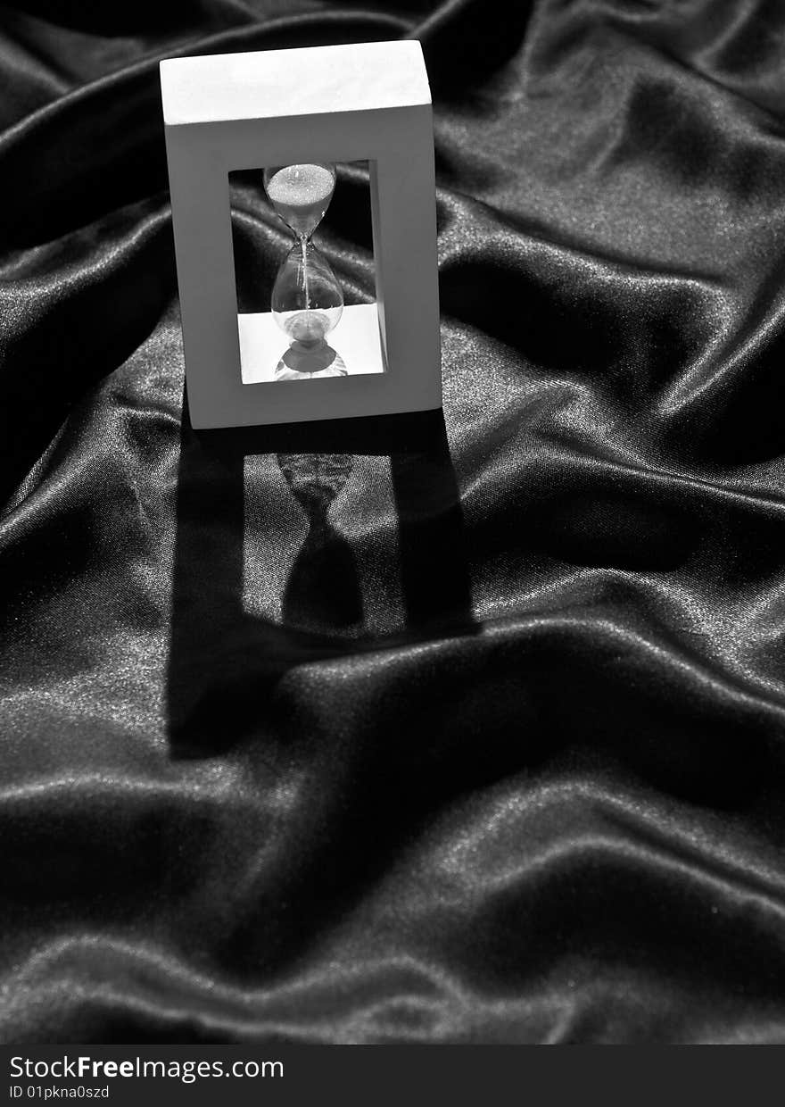 Still life of a backlighted hourglass on a crumpled black cloth, in black and white. Still life of a backlighted hourglass on a crumpled black cloth, in black and white