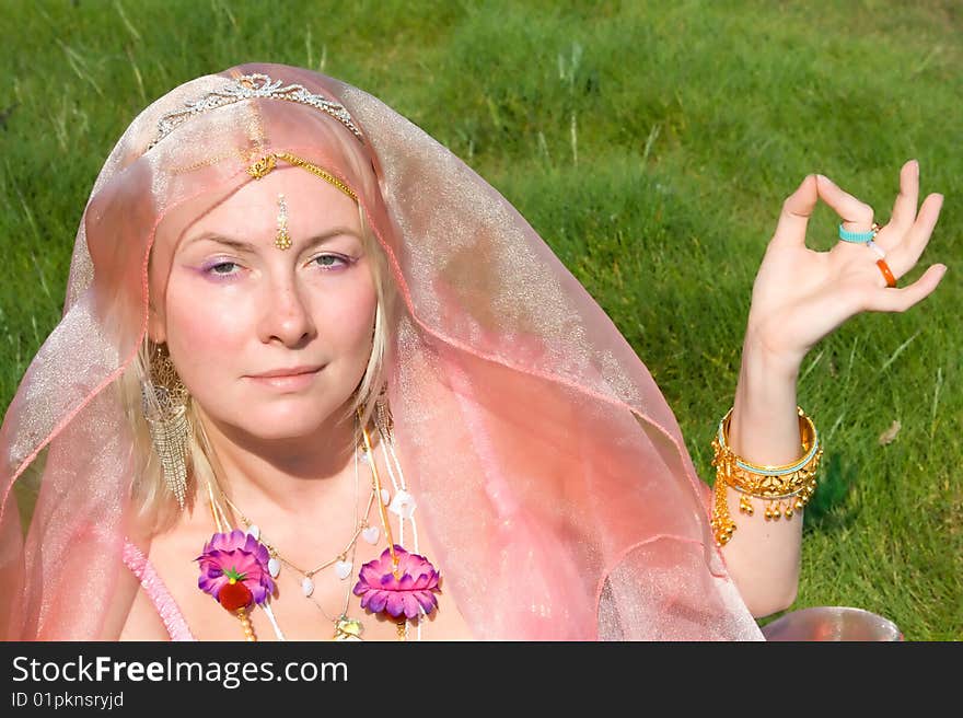 A woman in pink asian dress in meditation on a green grass