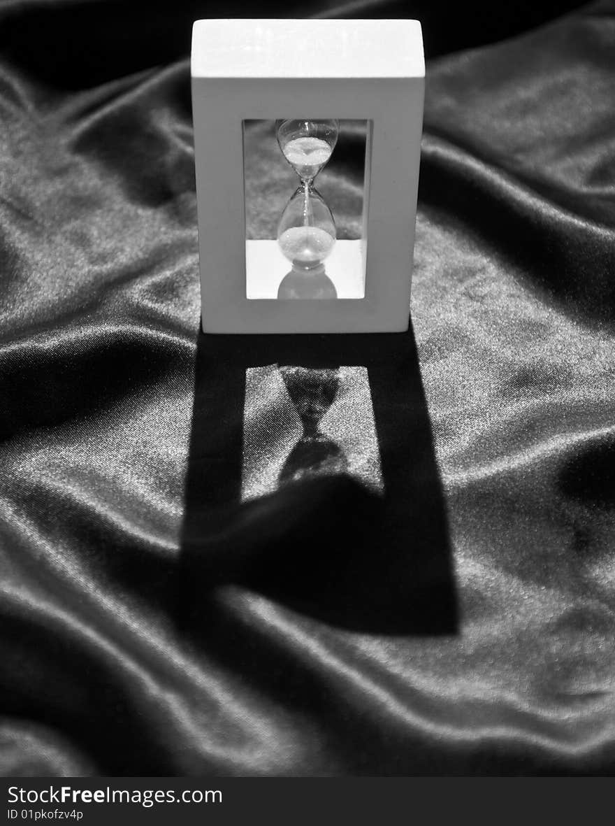 Still life of a backlighted hourglass on a crumpled black cloth, in black and white. Still life of a backlighted hourglass on a crumpled black cloth, in black and white