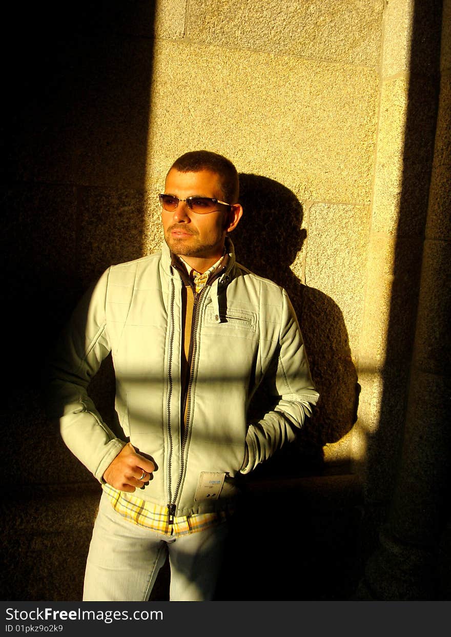 Male model with sunglasses on a brick stone wall half in the sun, half in the shadow. Male model with sunglasses on a brick stone wall half in the sun, half in the shadow