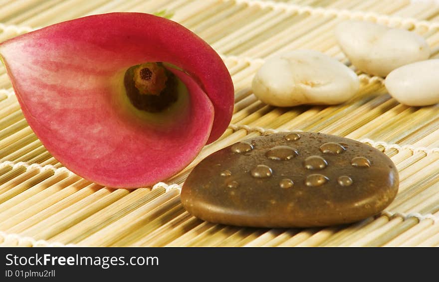 Pink calla blossom with stones on a bast mat