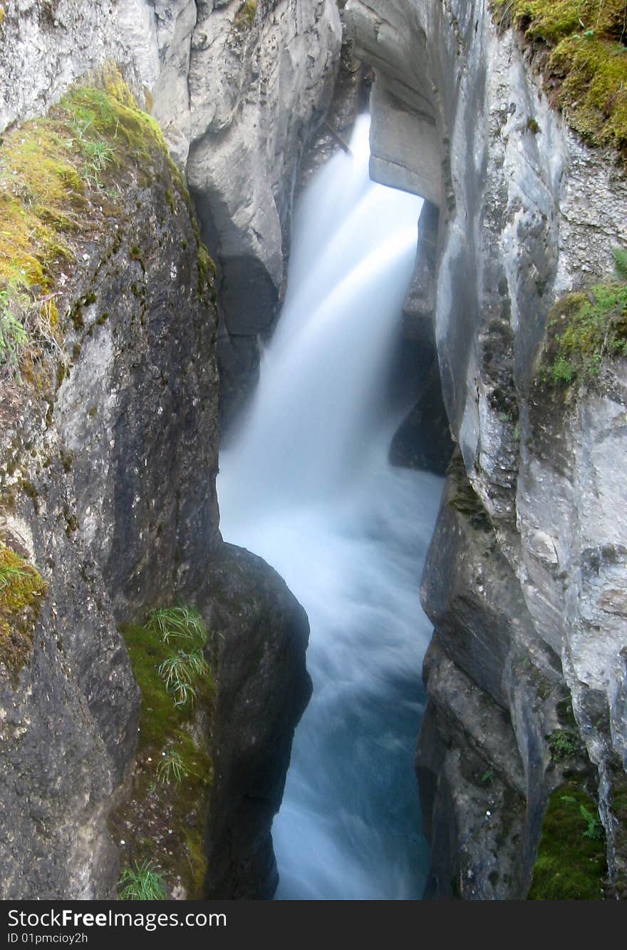 A blue and white waterfall cascading into a narrow canyon.