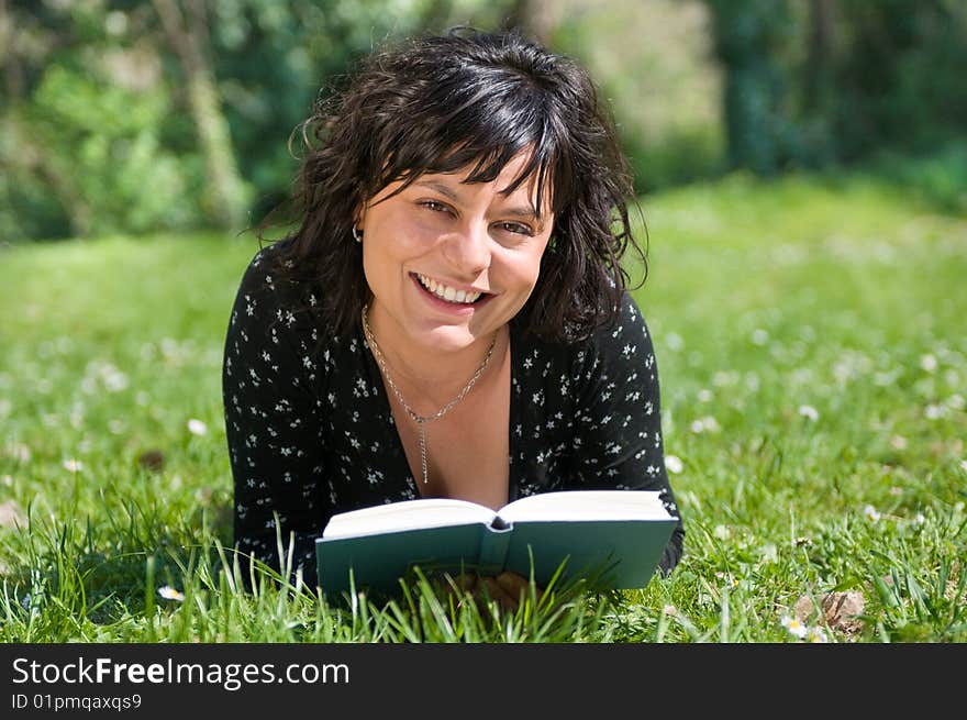 Smiling young woman lying on a flowery meadow reads a book. Smiling young woman lying on a flowery meadow reads a book