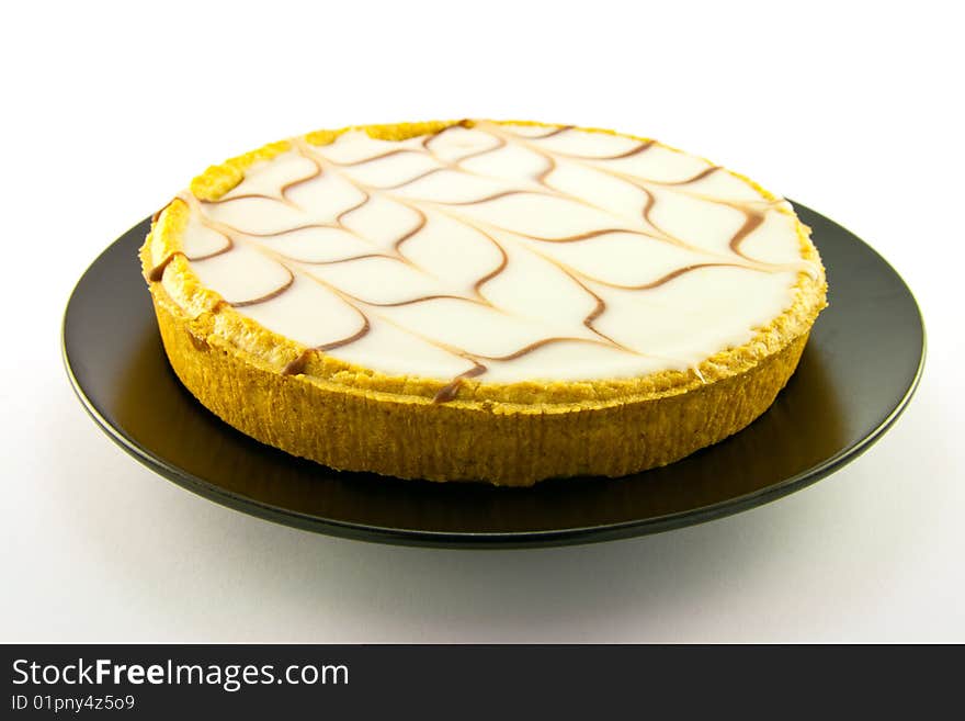 Delicious looking iced bakewell tart on a black plate with a plain background