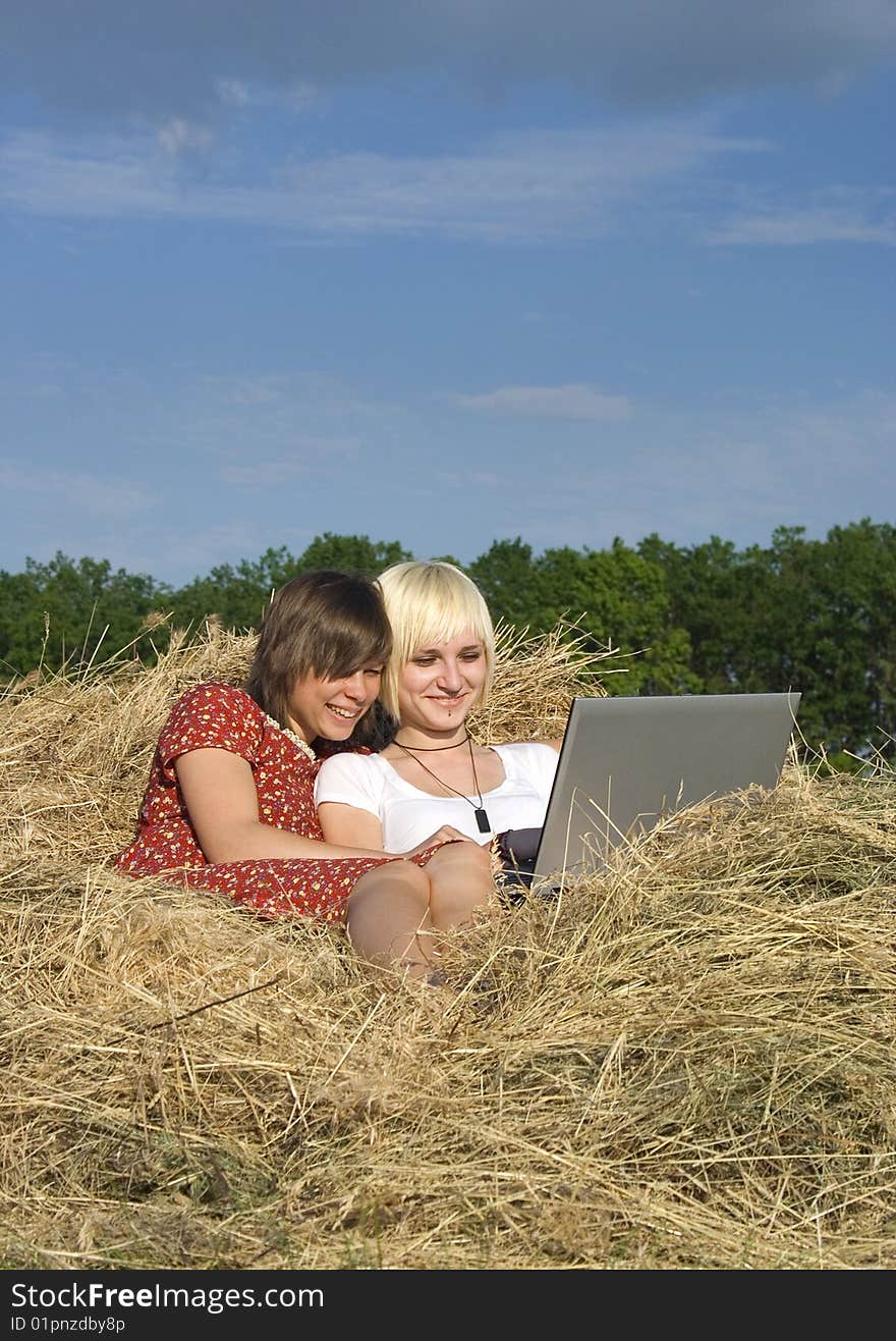 Two Young girl work with laptop in a stack of hay. Two Young girl work with laptop in a stack of hay