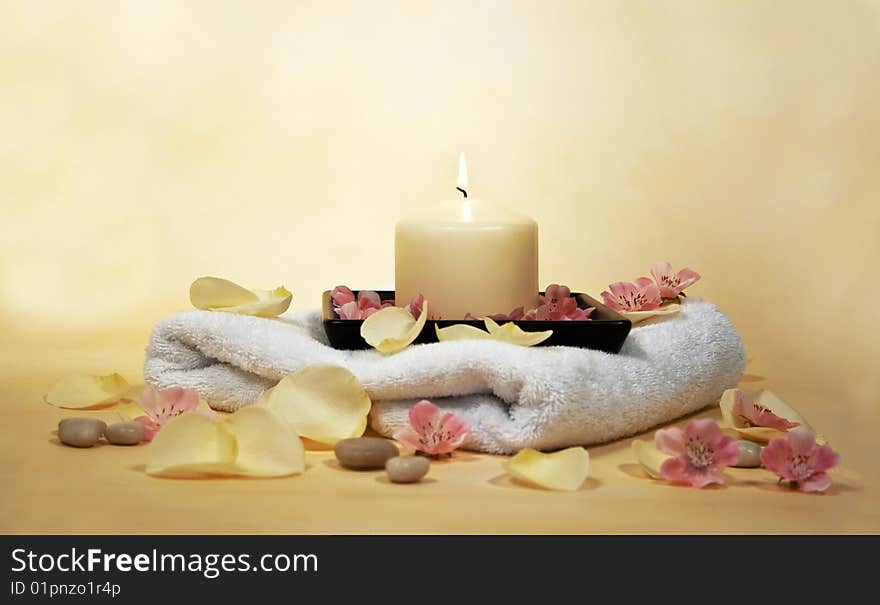 White towel with yellow candle and rose leaves and little stones. White towel with yellow candle and rose leaves and little stones