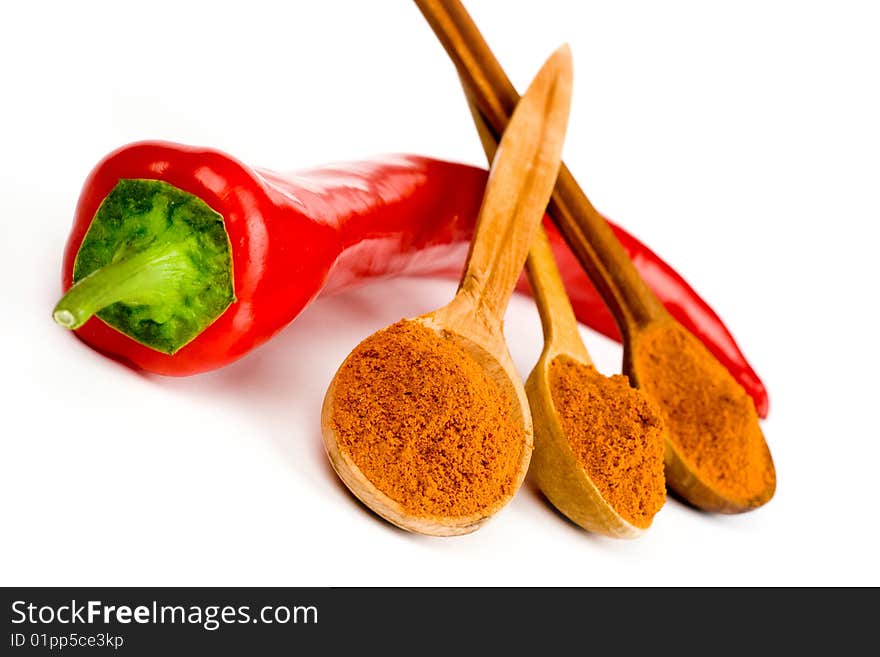 A composition of a pod of red hot  pepper and three wooden spoonful of ground red pepper on a white background. A composition of a pod of red hot  pepper and three wooden spoonful of ground red pepper on a white background