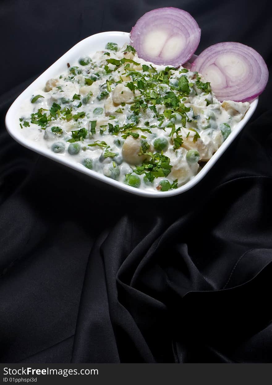 Photo of Pea potato salad with sliced onion on a black textured background. Photo of Pea potato salad with sliced onion on a black textured background