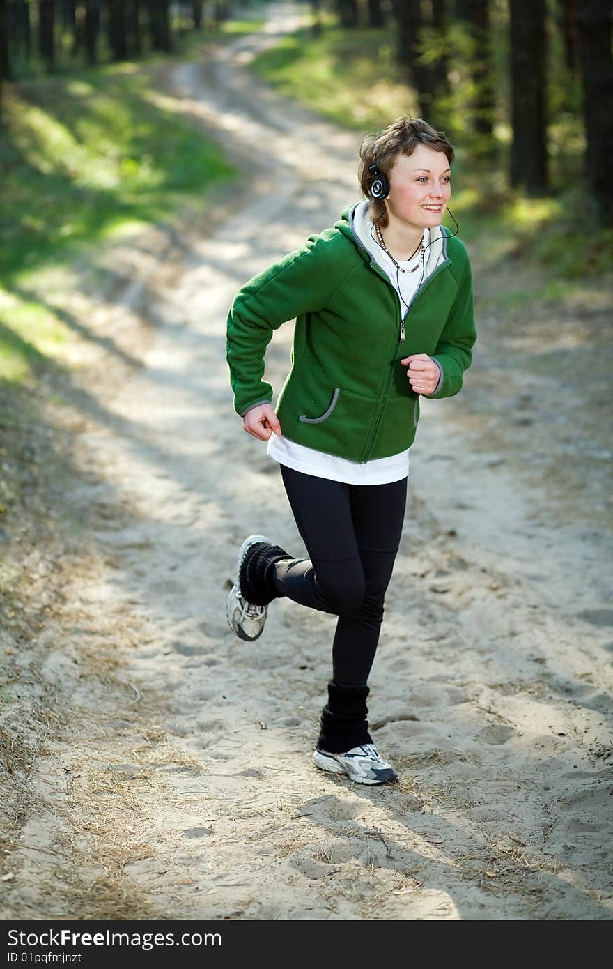 Pretty young girl runner in the forest while listening to music.