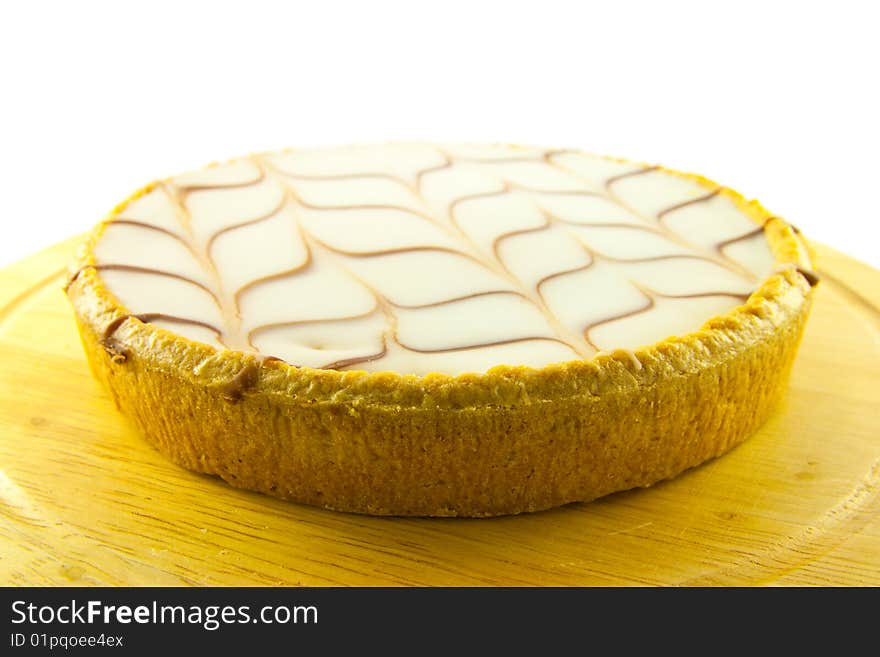 Delicious looking iced bakewell tart on a wooden platter with a plain background