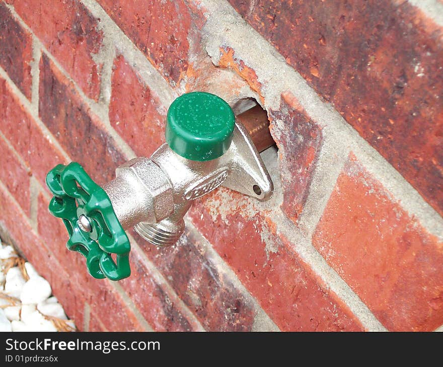 Green handled water spigot attached to a red-brick building. Green handled water spigot attached to a red-brick building.