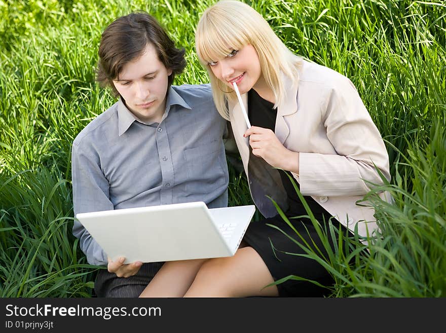 A young business man and business woman working on laptop in nature on the grass field. A young business man and business woman working on laptop in nature on the grass field