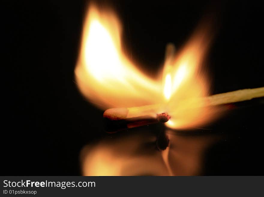 A match bursting into flames, isolated on a black reflective surface. A match bursting into flames, isolated on a black reflective surface