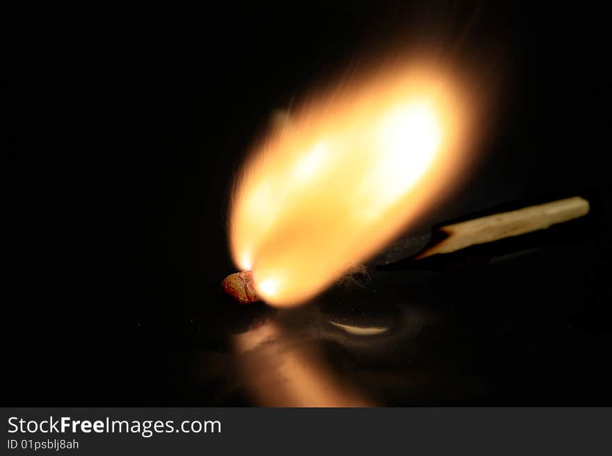 A match bursting into flames, isolated on a black reflective surface