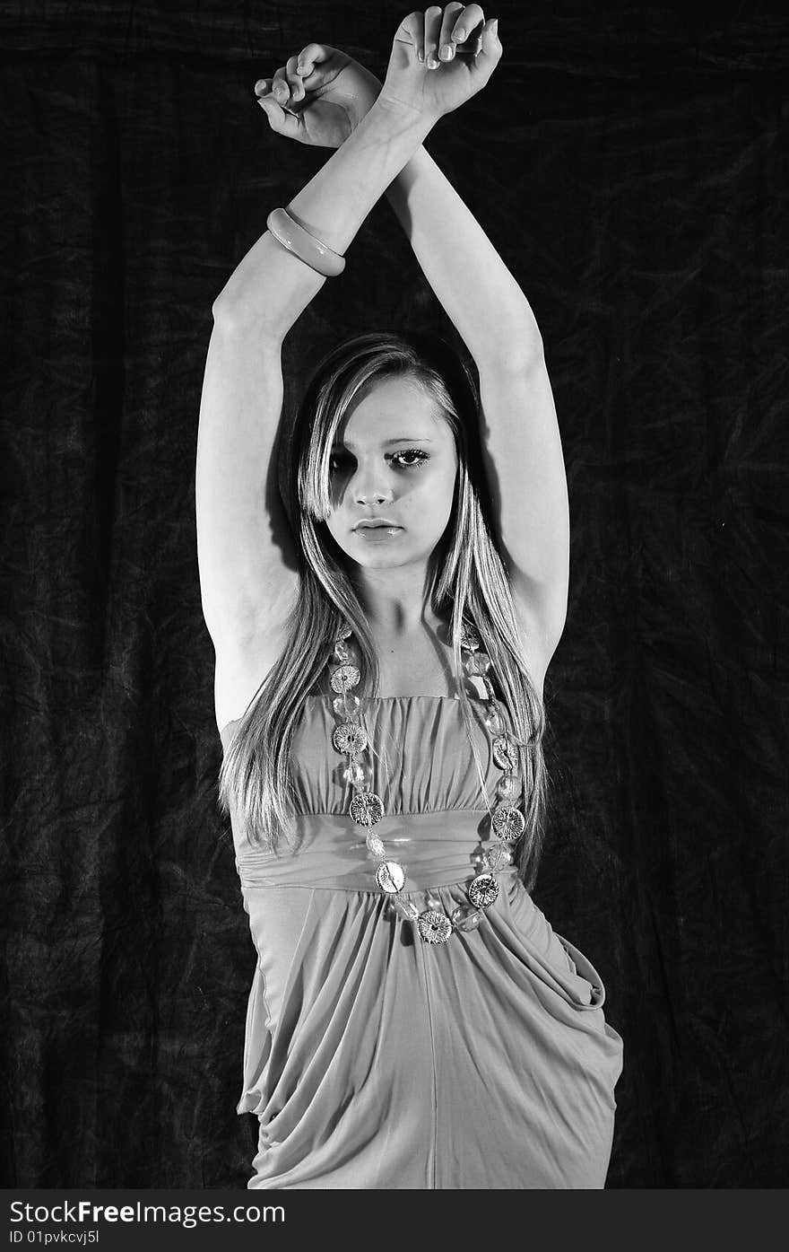 Young female fashion model holding her arms up crossed over her head looking at the camera against a charcoal back drop. Young female fashion model holding her arms up crossed over her head looking at the camera against a charcoal back drop.