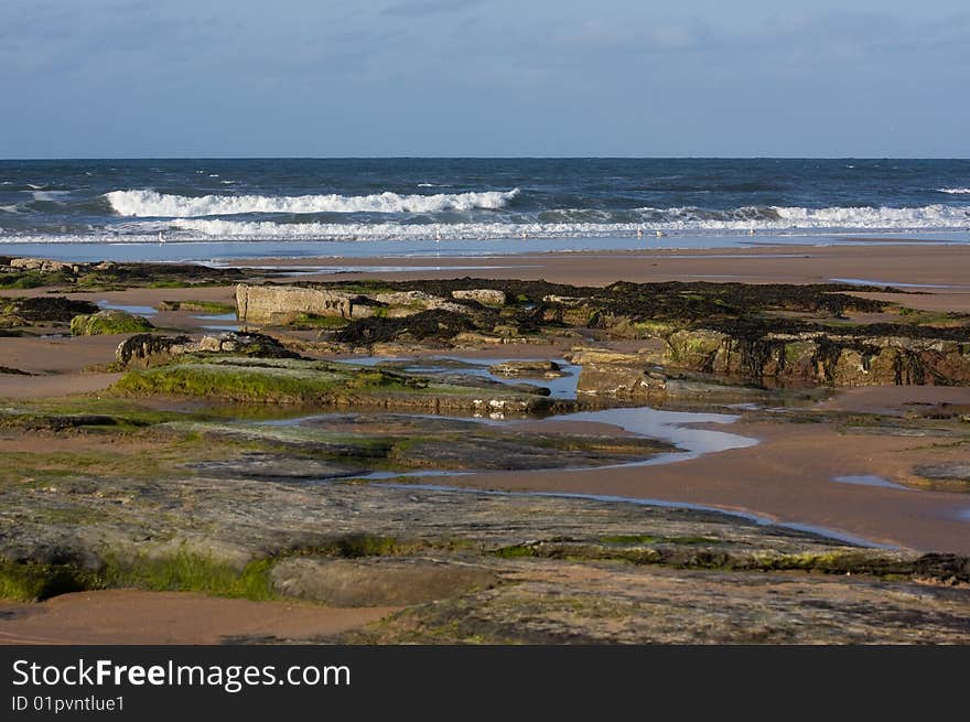 The surf is up, with sand and rocks in the foreground. The surf is up, with sand and rocks in the foreground