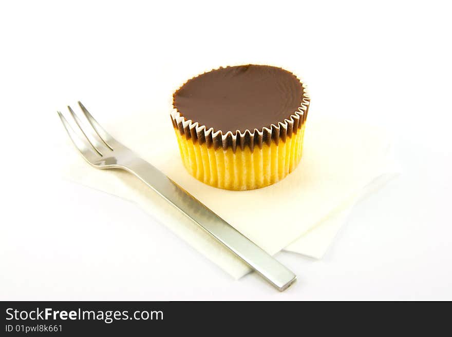 Delicious looking cup cake resting on two white napkins with a fork on a plain background