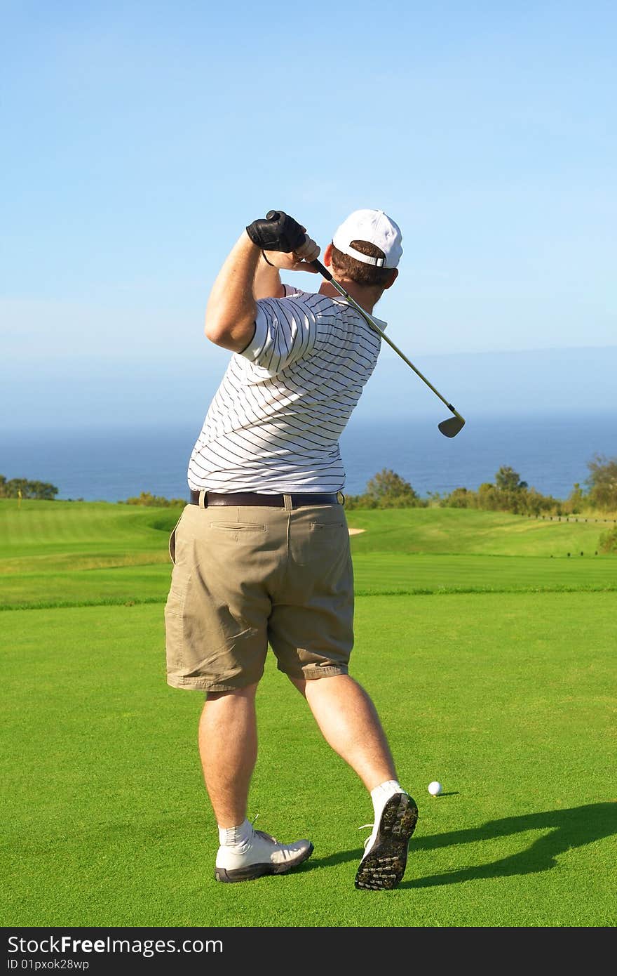 Young male golfer hitting the ball from the tee box next to the ocean on a beautiful summer day. Young male golfer hitting the ball from the tee box next to the ocean on a beautiful summer day