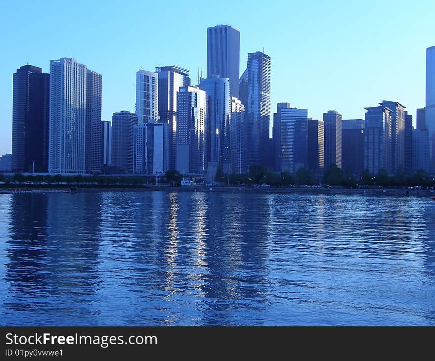 A cityscape by a lake in blue hues. A cityscape by a lake in blue hues