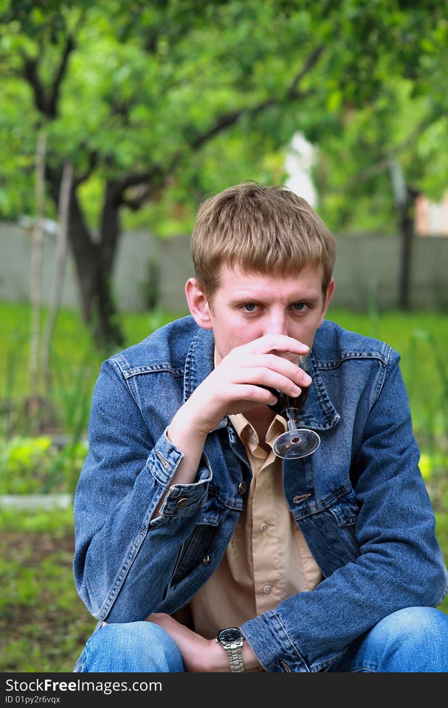 Young men in jeans jacket with glass of red wine in the garden. Young men in jeans jacket with glass of red wine in the garden