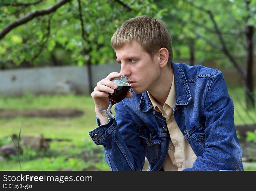 Young men in jeans jacket with glass of red wine in the garden. Young men in jeans jacket with glass of red wine in the garden