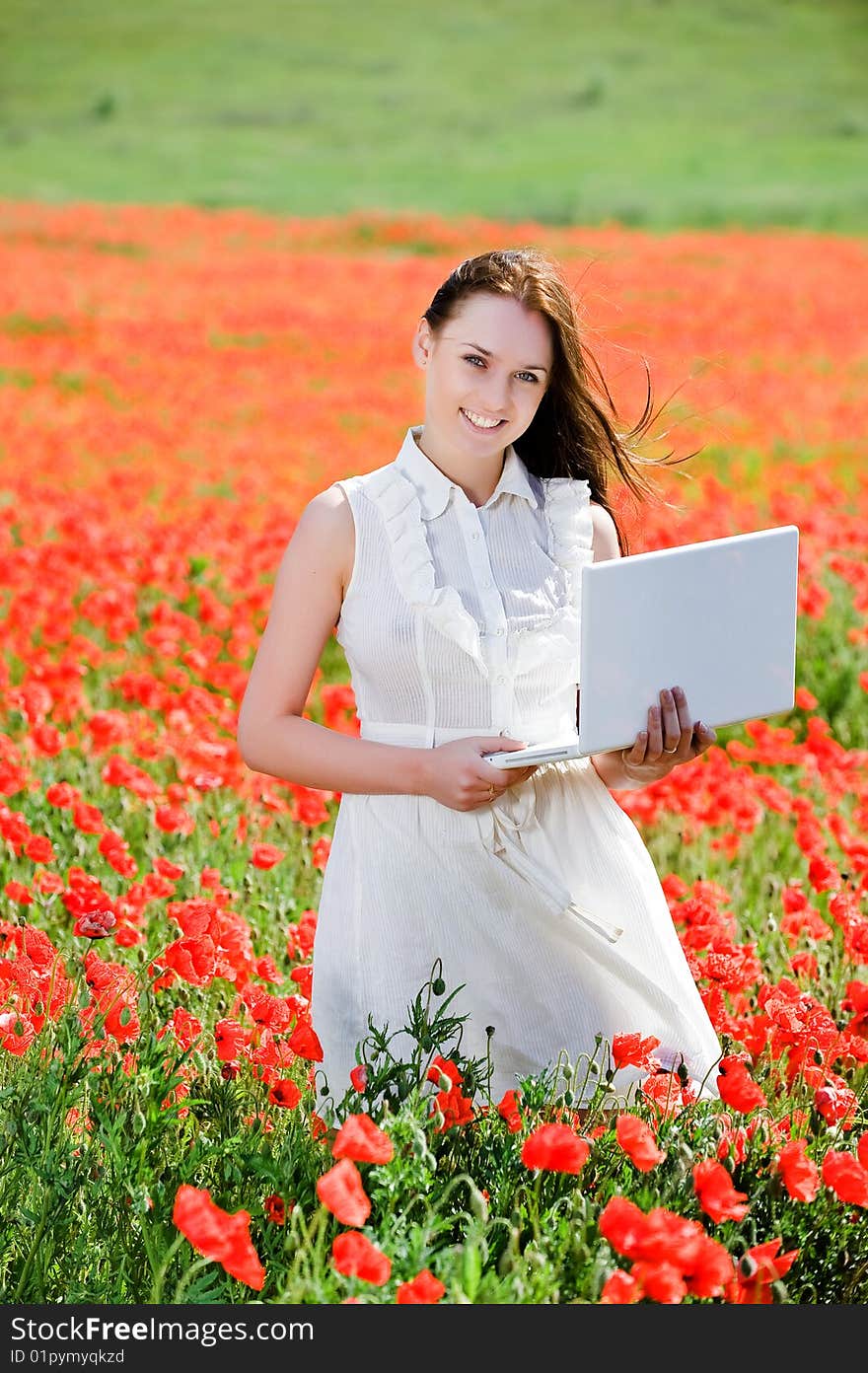 Attractive smiling girl with laptop in the poppy field