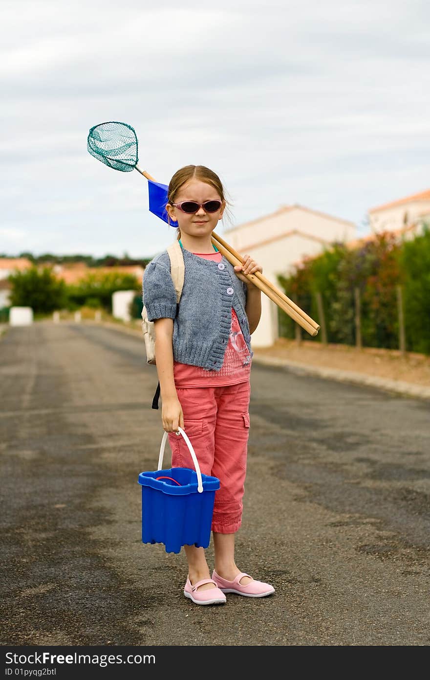 A girl pauses as she walks to the beach with a bucket, shovel, and net. A girl pauses as she walks to the beach with a bucket, shovel, and net.