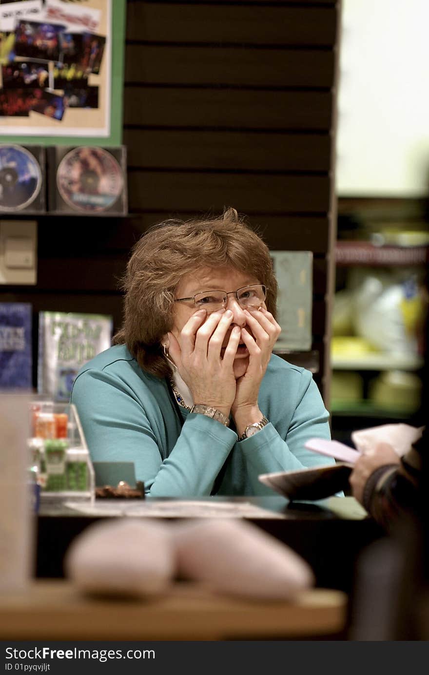 Older woman behind book sales counter looking perplexed with both hands up to face. Older woman behind book sales counter looking perplexed with both hands up to face.