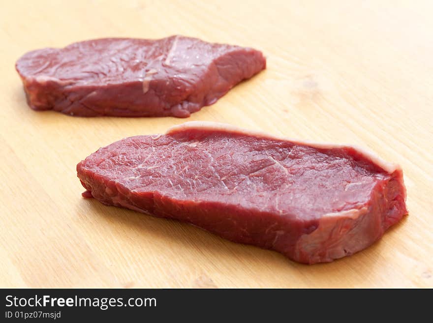 Uncooked steaks on wooden cutting board