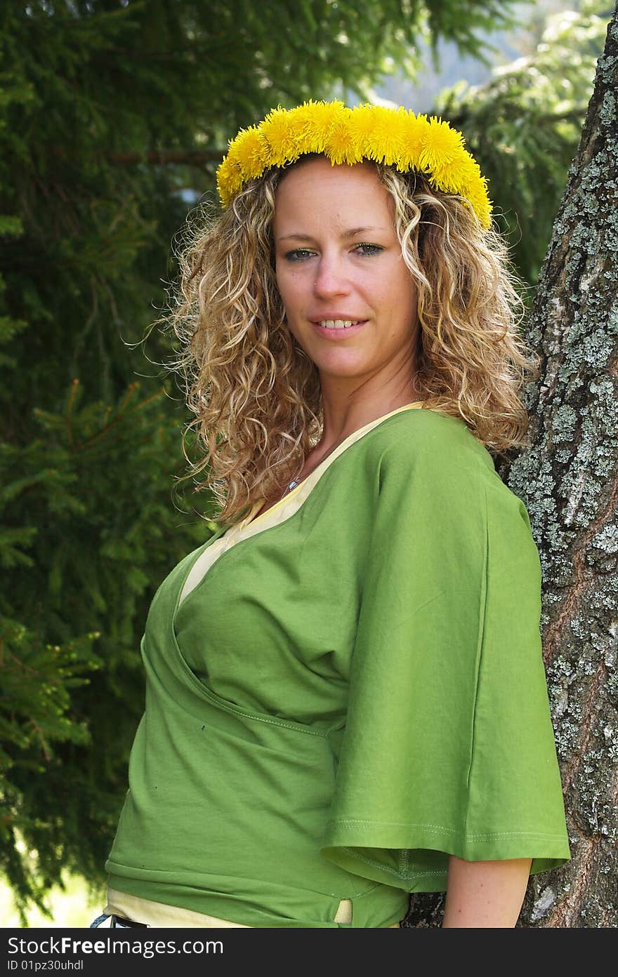 Curly girl with dandelion chain on head standing by birch tree