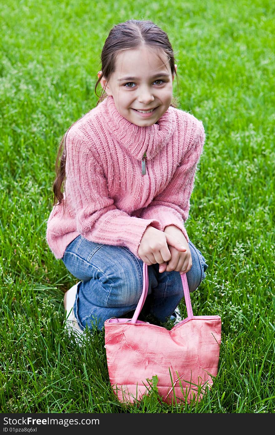 Girl in a pink sweater sits on a green grass