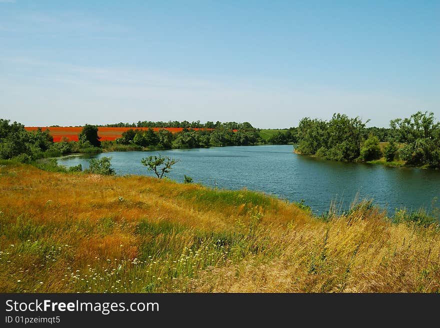 Sun specks of light on water and red poppy field on horizon. Sun specks of light on water and red poppy field on horizon