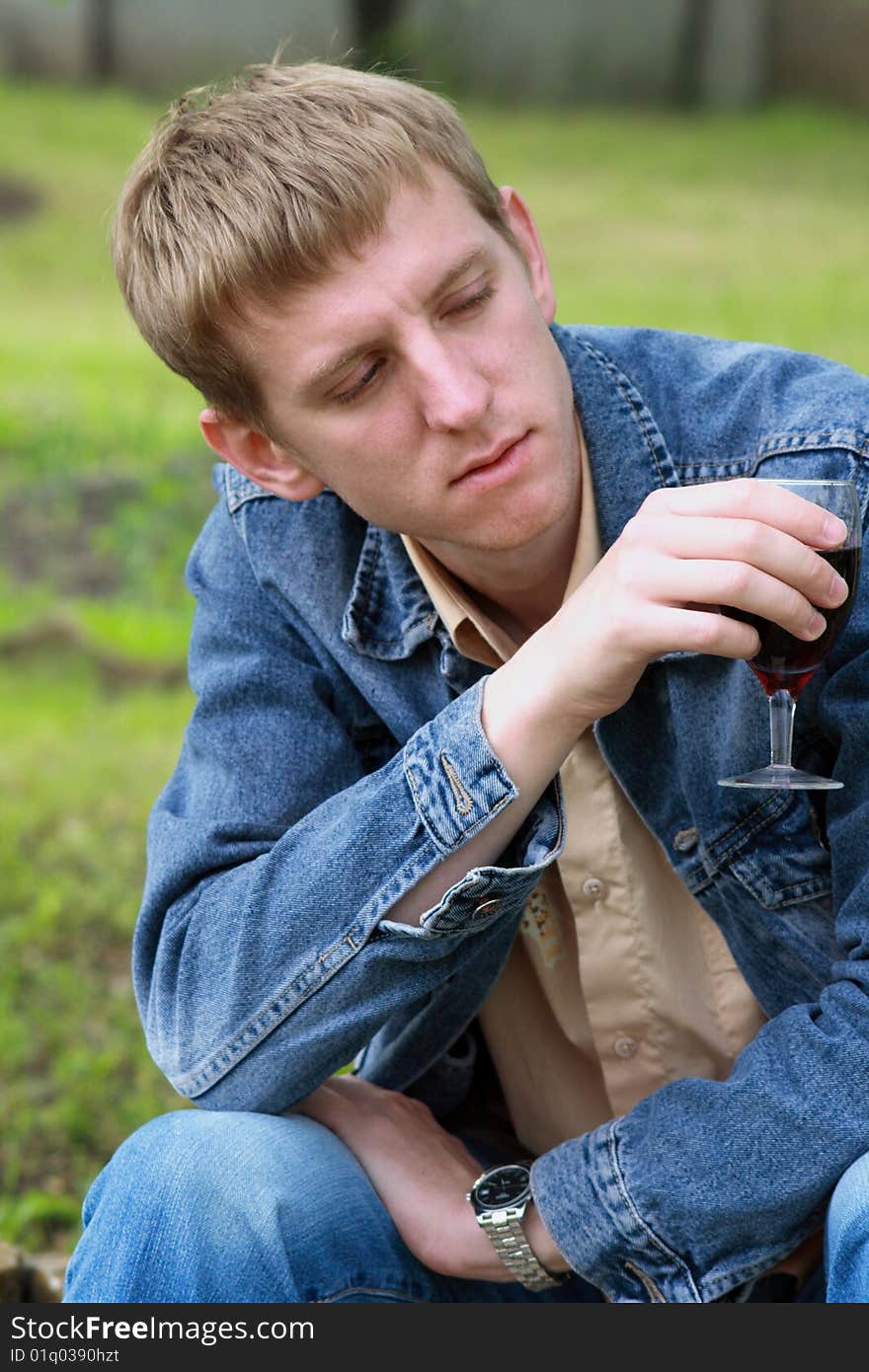 Young men in jeans jacket with glass of red wine in the garden. Young men in jeans jacket with glass of red wine in the garden