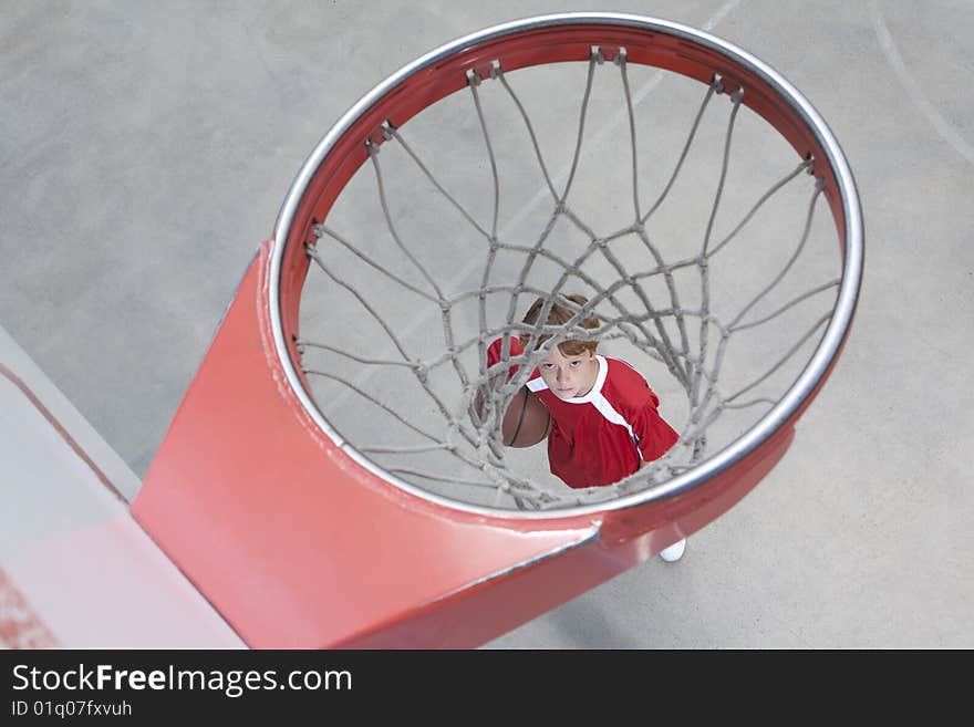 Boy standing looking up through basketball hoop. Boy standing looking up through basketball hoop